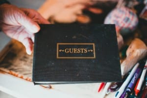 A black guest book with gold lettering, accompanied by a hand.