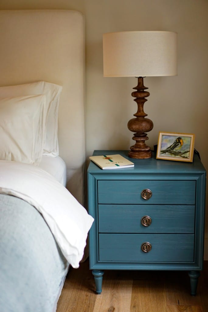 A blue nightstand with a lamp on top, next to a bed